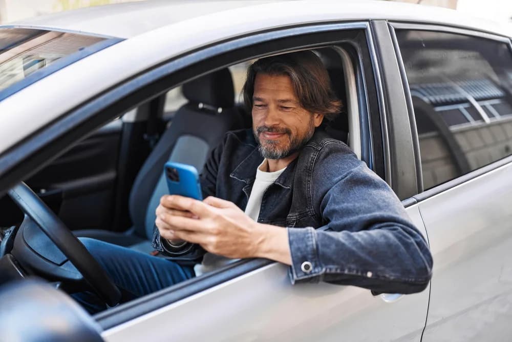 Řidič kontroluje aplikaci na telefonu ve svém autě.