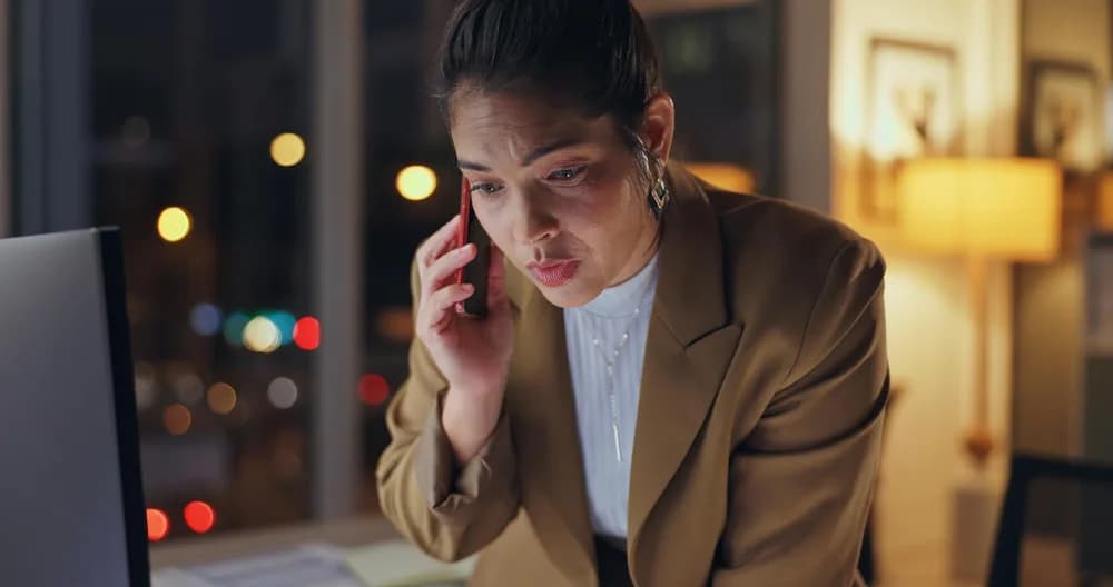 Žena večer telefonuje u notebooku a tváří se ustaraně.