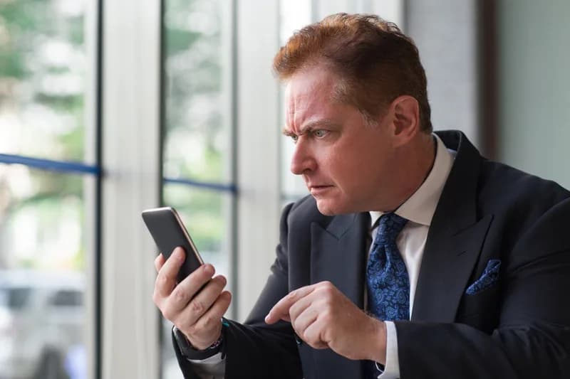 Překvapený manažer čte zprávu v mobilním telefonu.