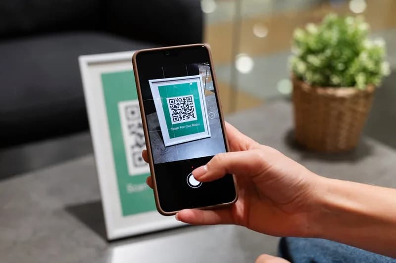 Člověk skenuje telefonem QR kód na stole.